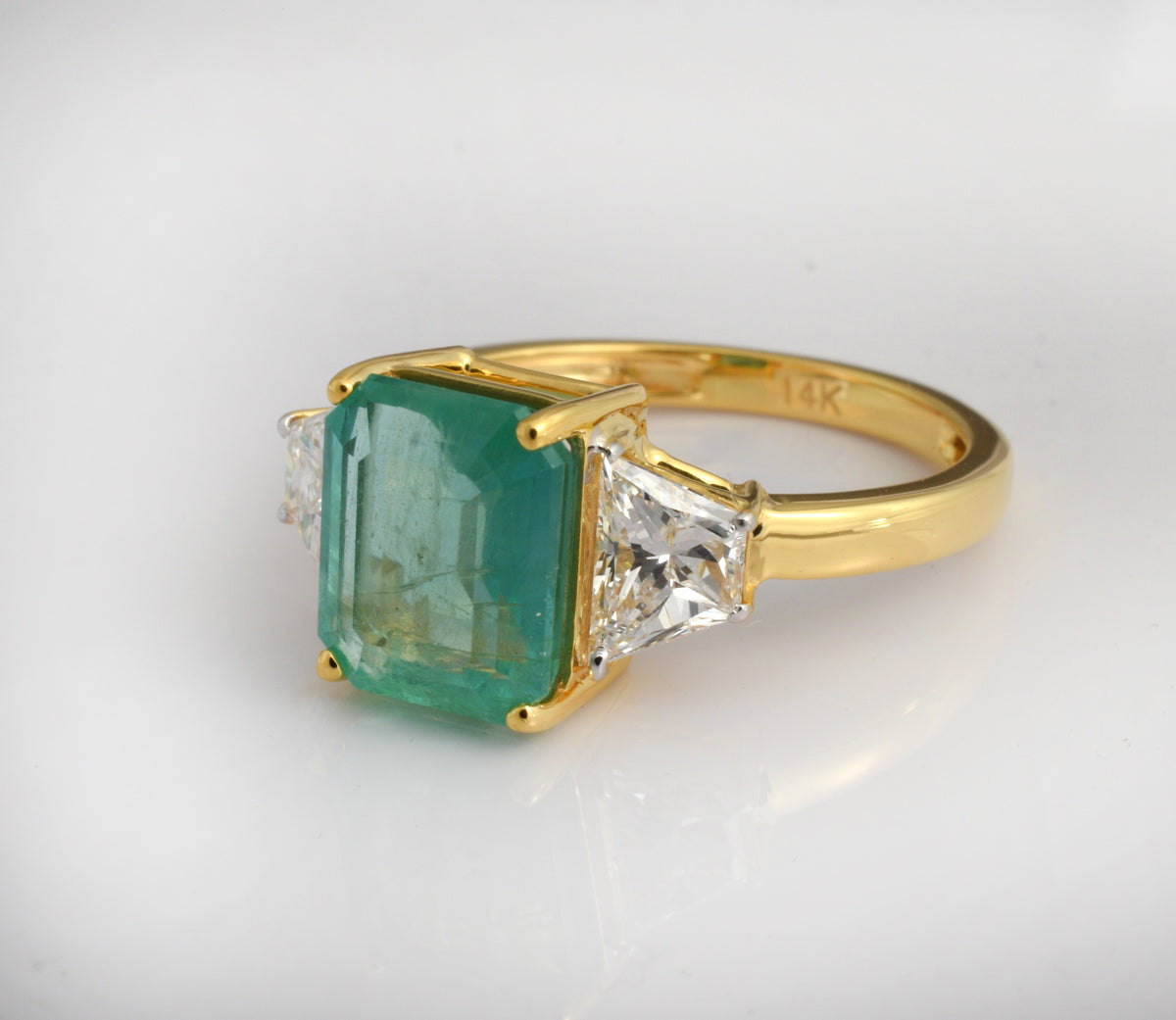 Emerald cut emerald engagement ring in 14K yellow gold with three diamonds, showcasing luxury green gemstone jewelry.