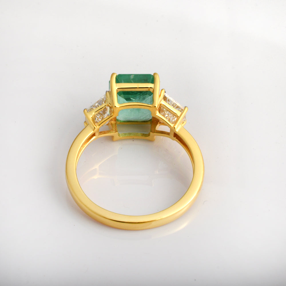 Emerald cut emerald engagement ring with three diamonds in 14K yellow gold, featuring a luxurious green gemstone design.