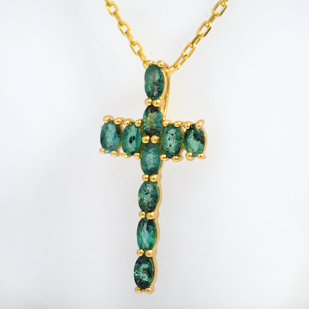 A gold cross pendant necklace featuring a series of green emerald-cut gemstones, shown against a plain white background.