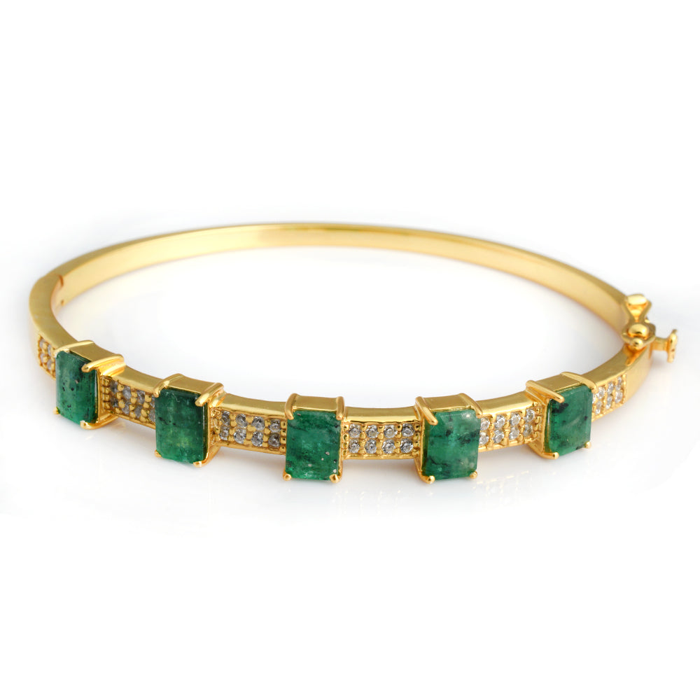 A gold bangle bracelet featuring five rectangular green emerald-cut gemstones and rows of small clear accent stones, shown on a plain white background.