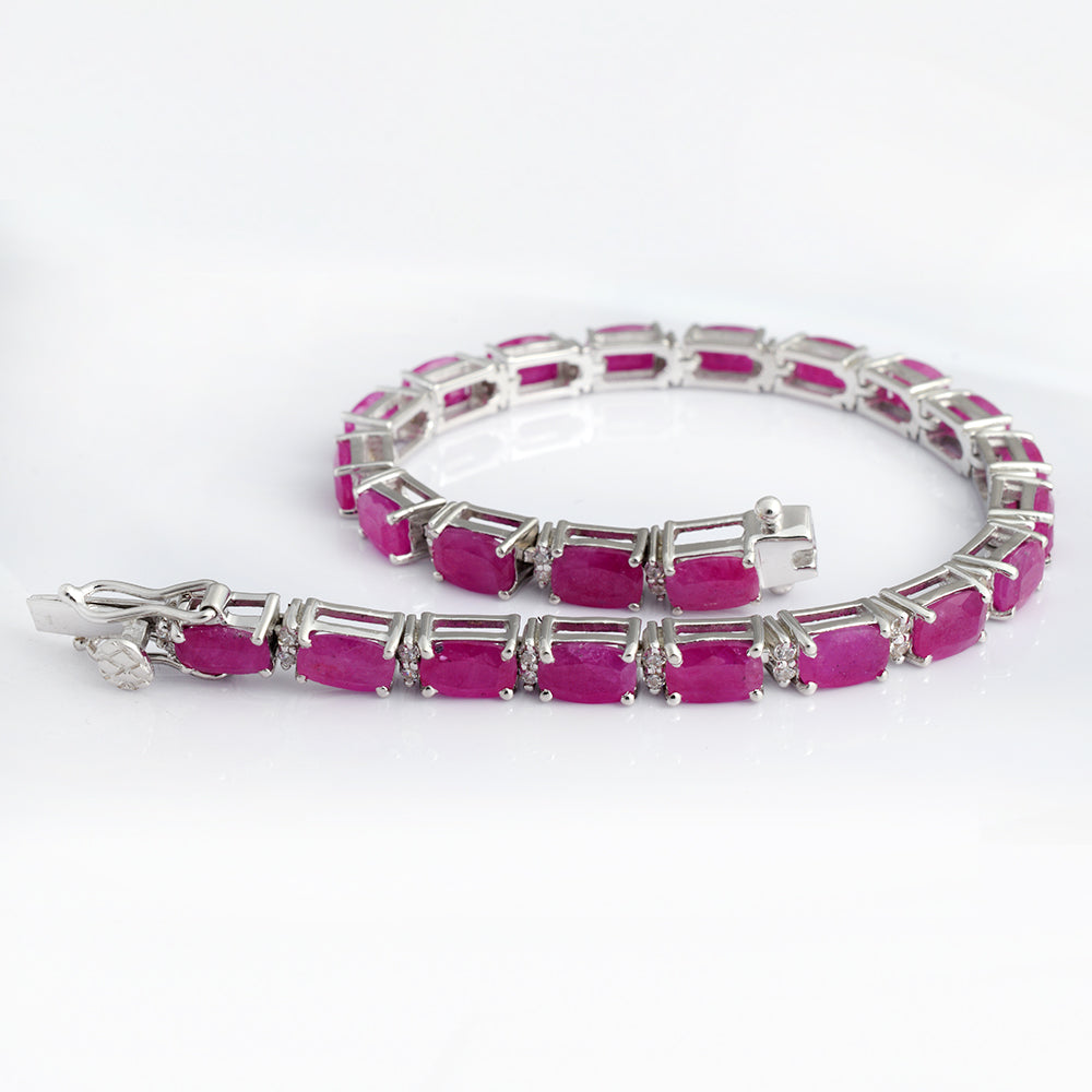 A tennis bracelet featuring rectangular pinkish-red gemstones set in a silver-toned metal, displayed on a clean white background.