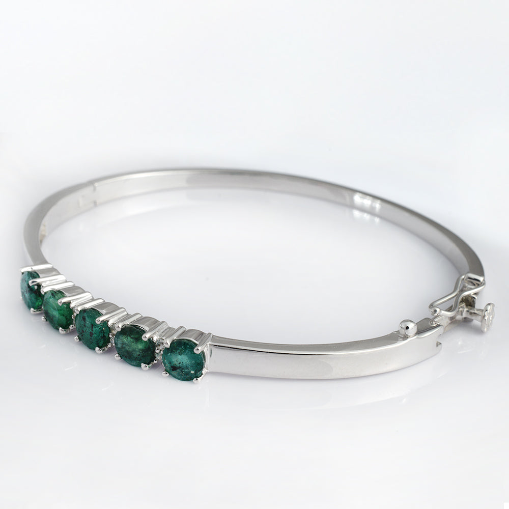 A polished silver bangle bracelet featuring a row of five round-cut green emerald-cut gemstones in a prong setting, displayed on a clean white background.