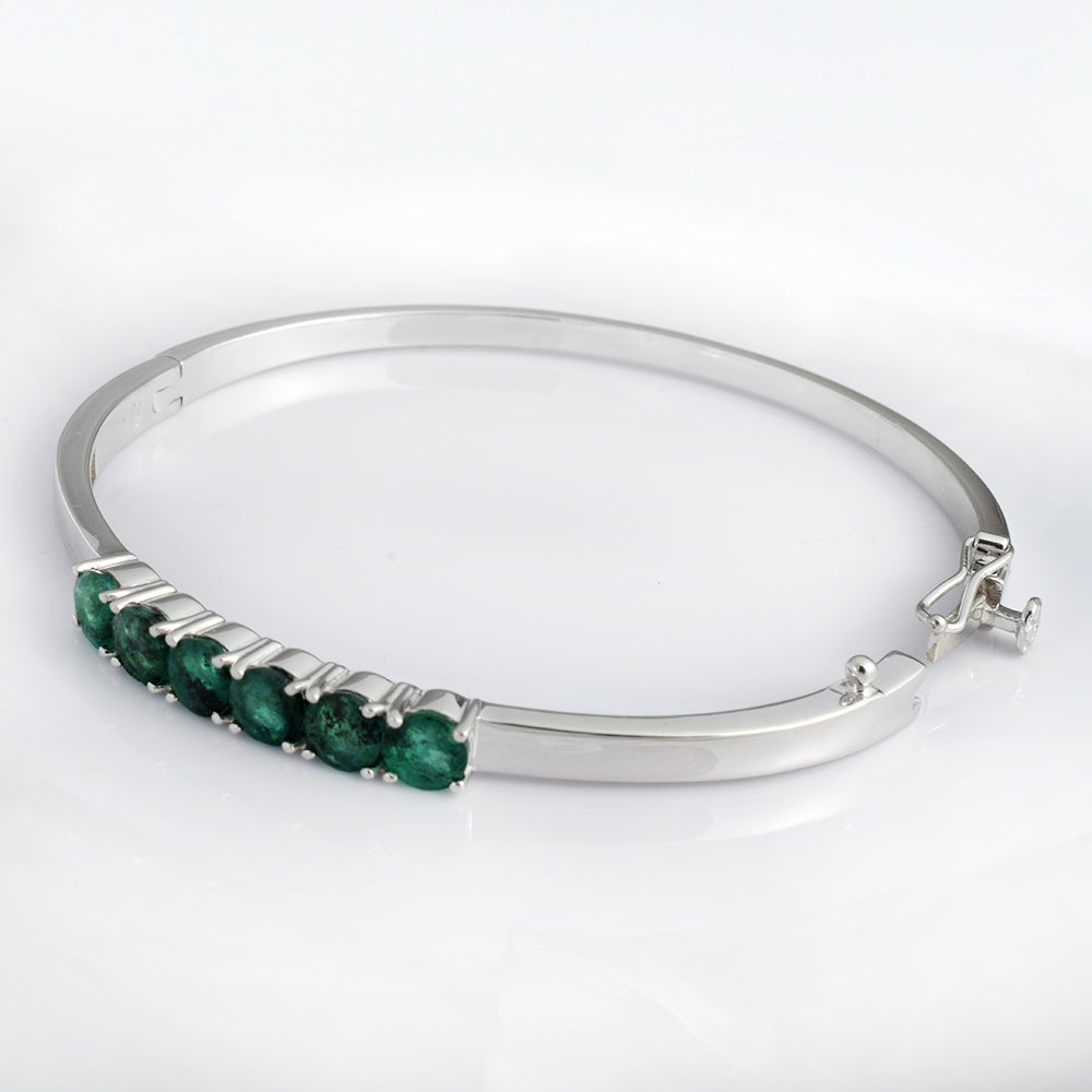 A polished silver-tone bangle bracelet featuring a row of round-cut green emeralds along the front, displayed on a clean white background.