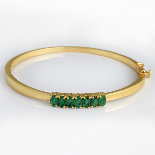A gold bangle bracelet featuring a row of round green emerald-cut gemstones set in a gold bezel, shown on a clean white background.