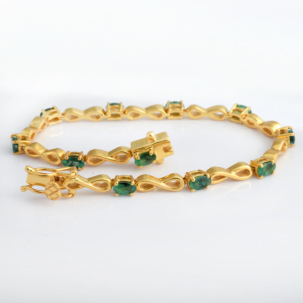 A gold infinity-link bracelet with small green gemstone accents, displayed on a clean white background.