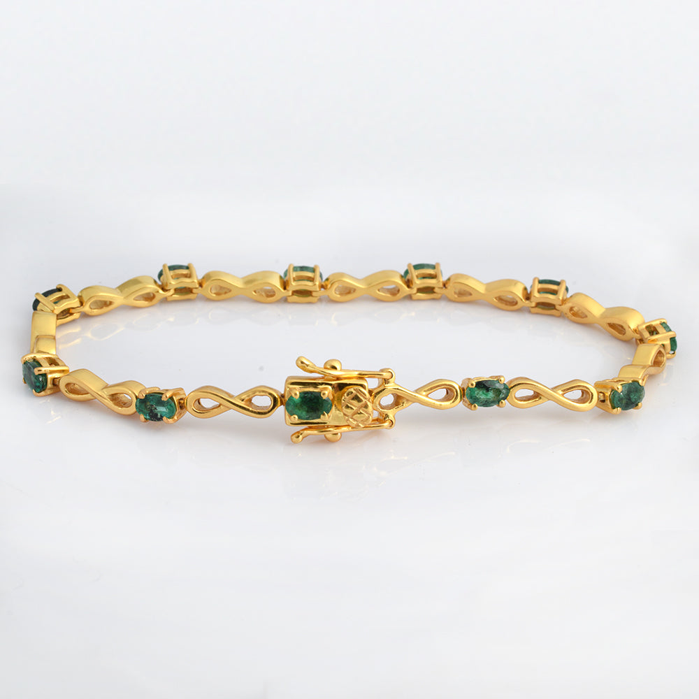 A yellow gold tennis bracelet featuring round-cut green emerald-cut gemstones set in decorative links, with a central floral motif and clasp, shown on a white background.
