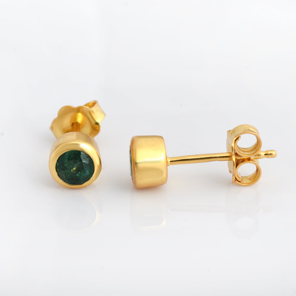 A pair of gold stud earrings with round green gemstones, shown from both front and side angles on a white reflective surface.