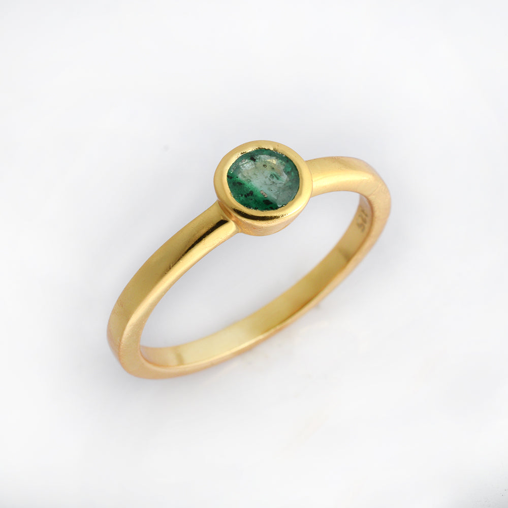 A gold ring with a round green gemstone in a bezel setting, photographed on a clean white background.